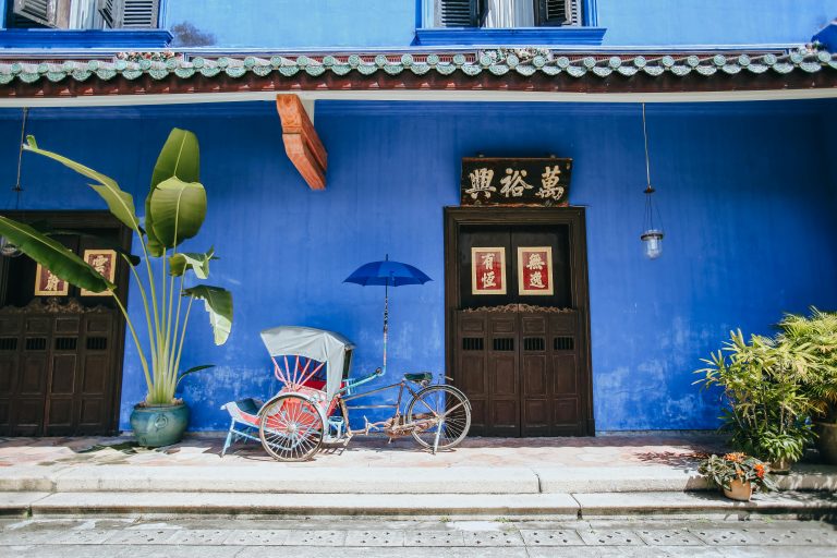 Traditional rickshaw and blue facade in George Town, Penang, Malaysia capturing cultural essence.