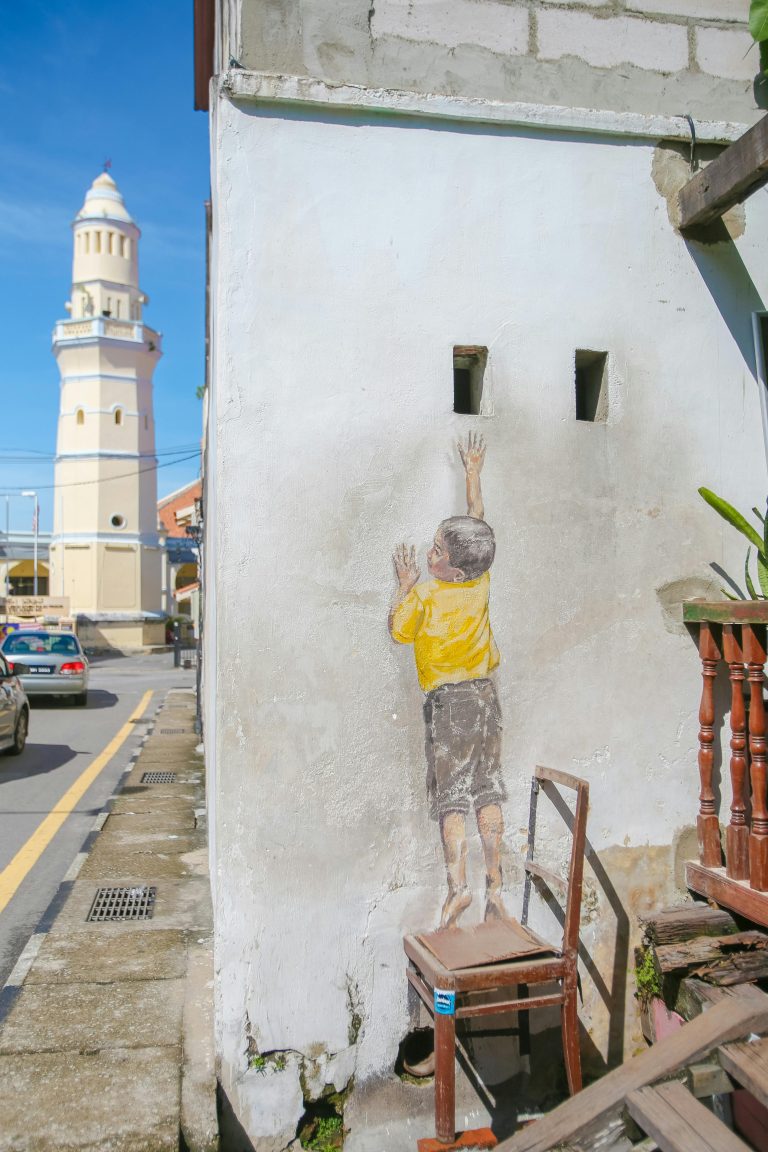 Street art on a building in George Town, Penang, showing a boy reaching up. Features local architecture.