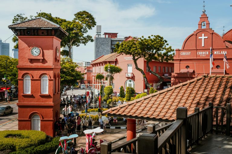 Vibrant scene of Malacca's iconic Christ Church and its bustling surroundings on a bright day.