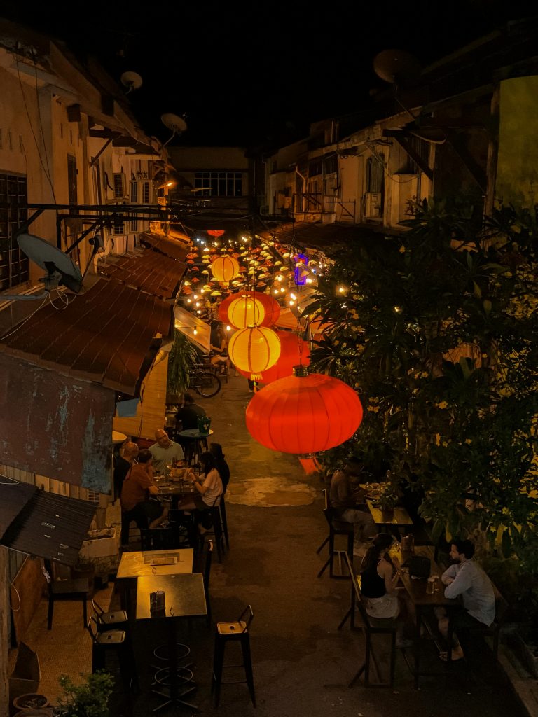 A festive Asian alley at night illuminated by hanging red and yellow lanterns.